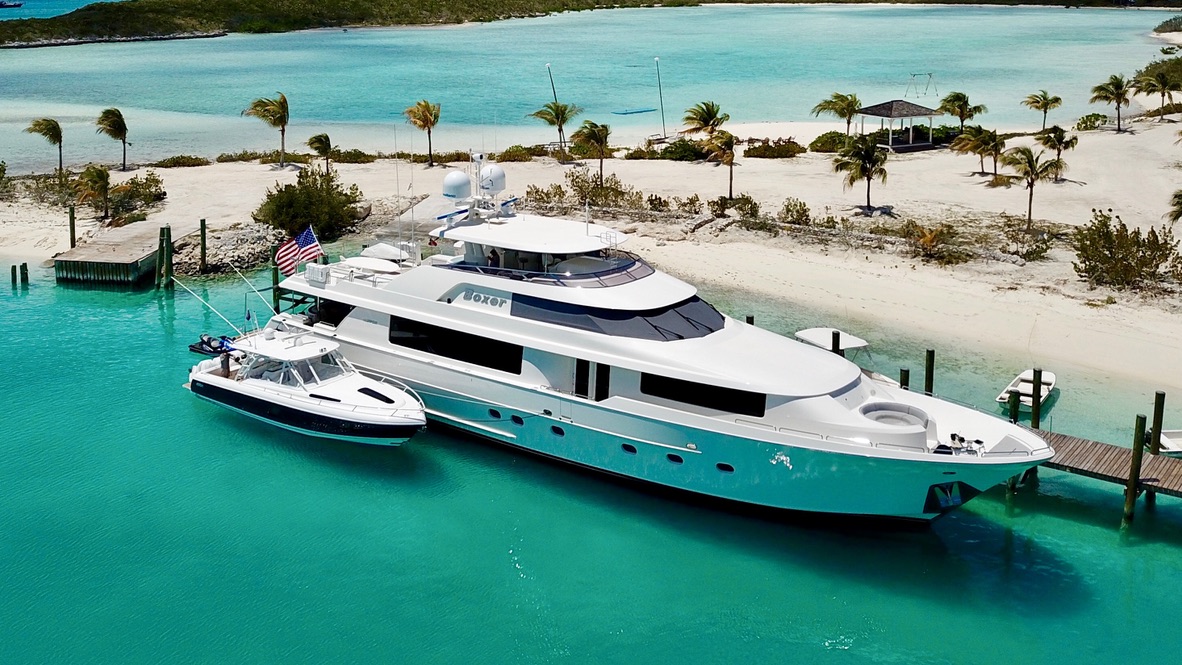 Boxer lying alongside a beach dock in the Bahamas with her tender, flying a United States ensign