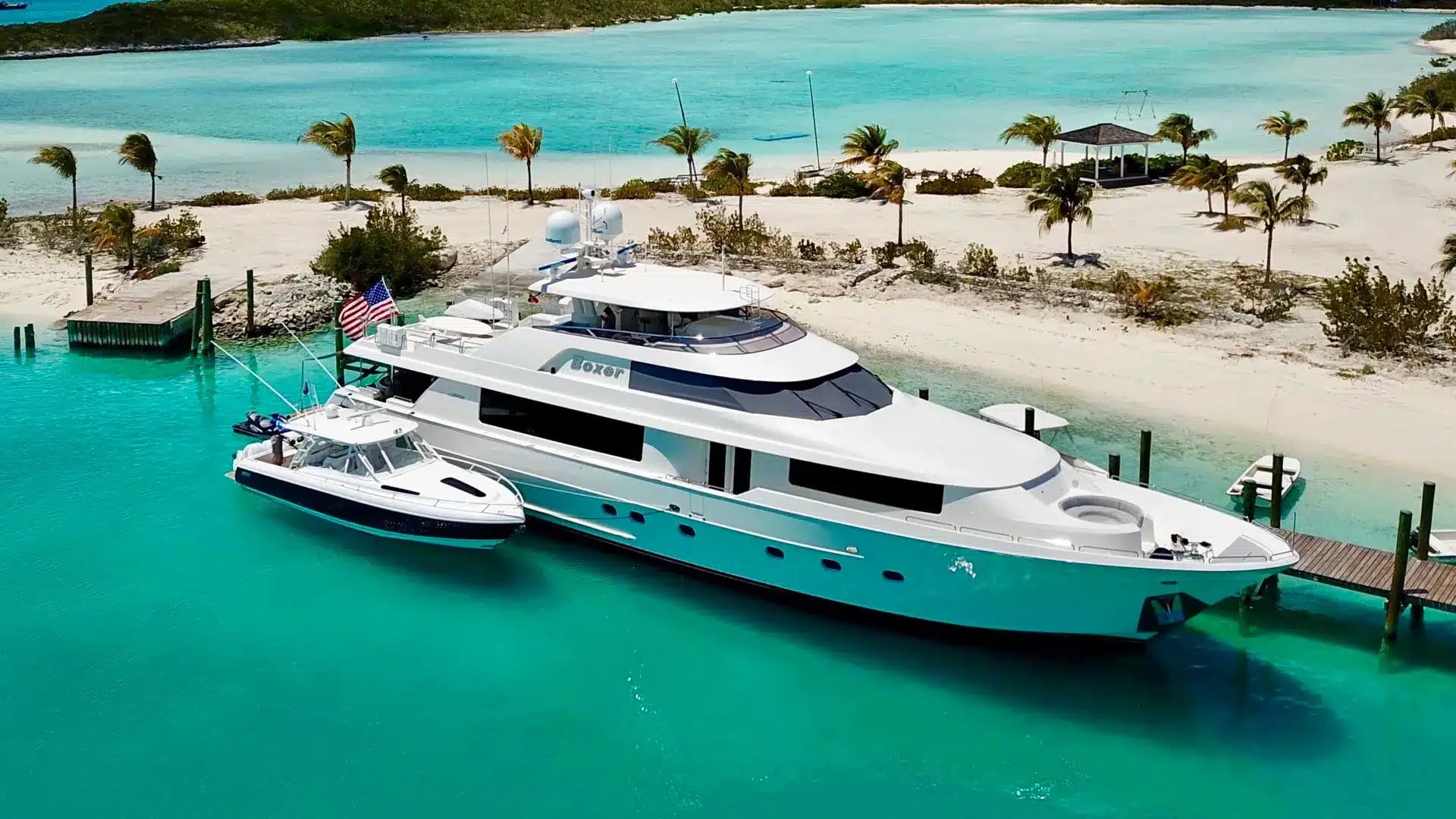 A motor yacht and her tender off a white-sand beach