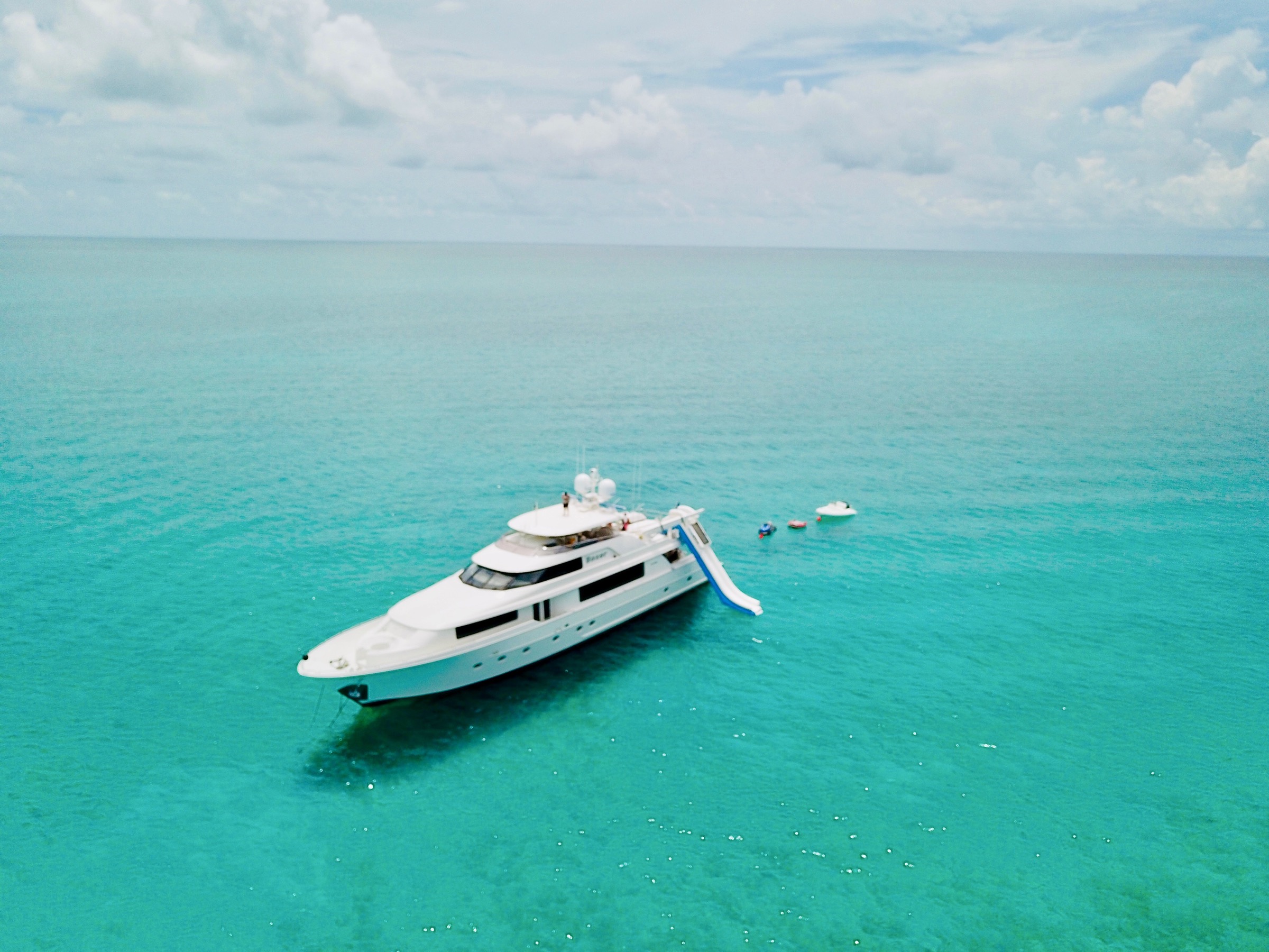 A motor yacht lying at anchor on flat turquoise water in the Bahamas, her tender alongside